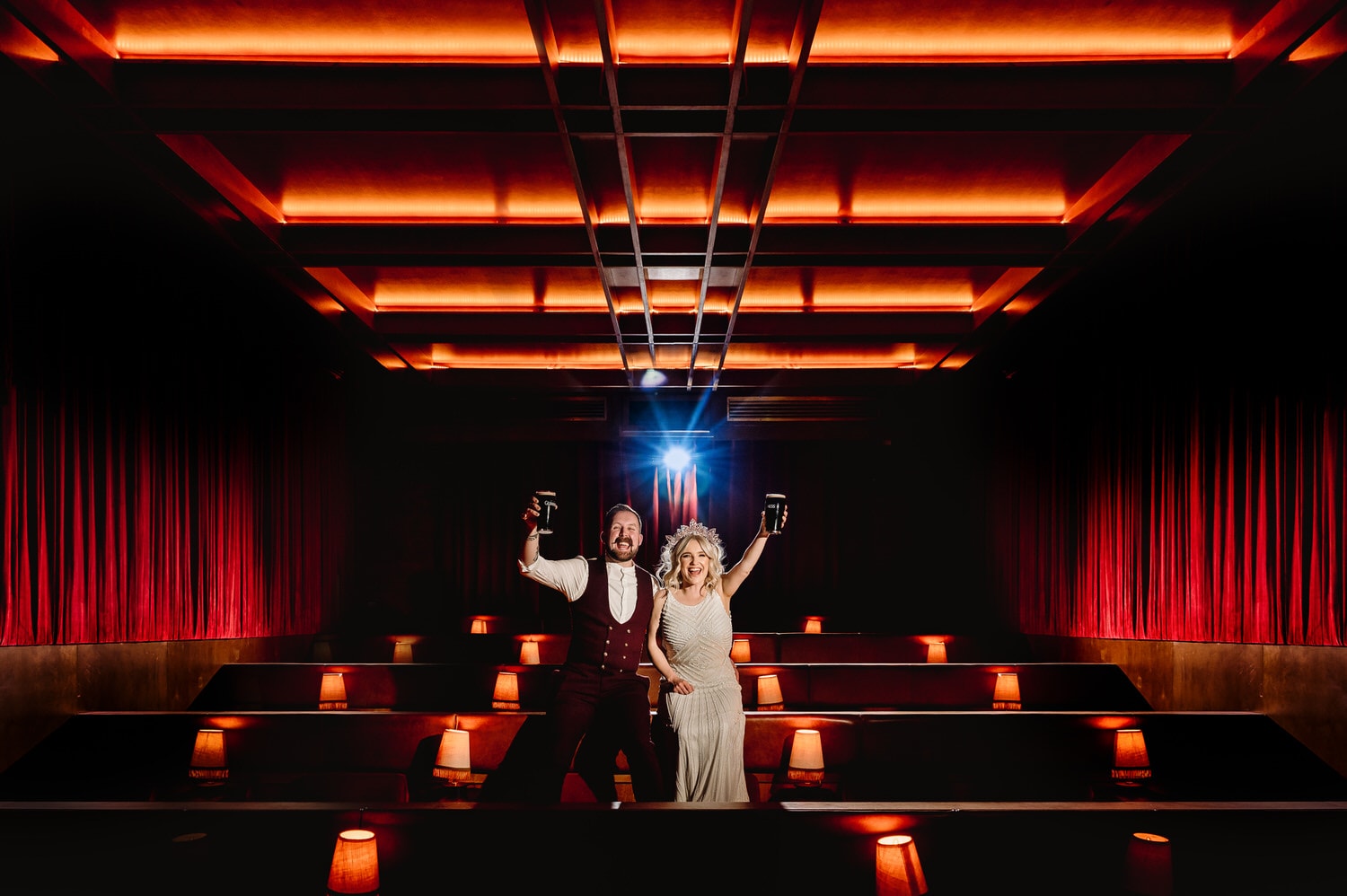 Wedding couple laughing and holding up pints of Guinness in a private cinema located in the basement of The Devlin Hotel, Dublin. 