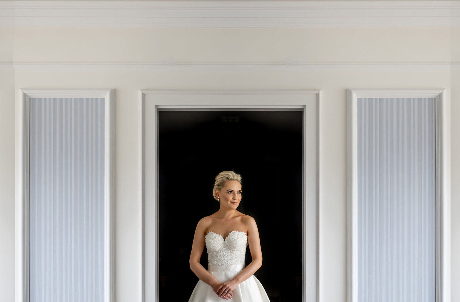 Posed photograph of a blond bride standing within a dark door frame at Powerscourt Hotel. 