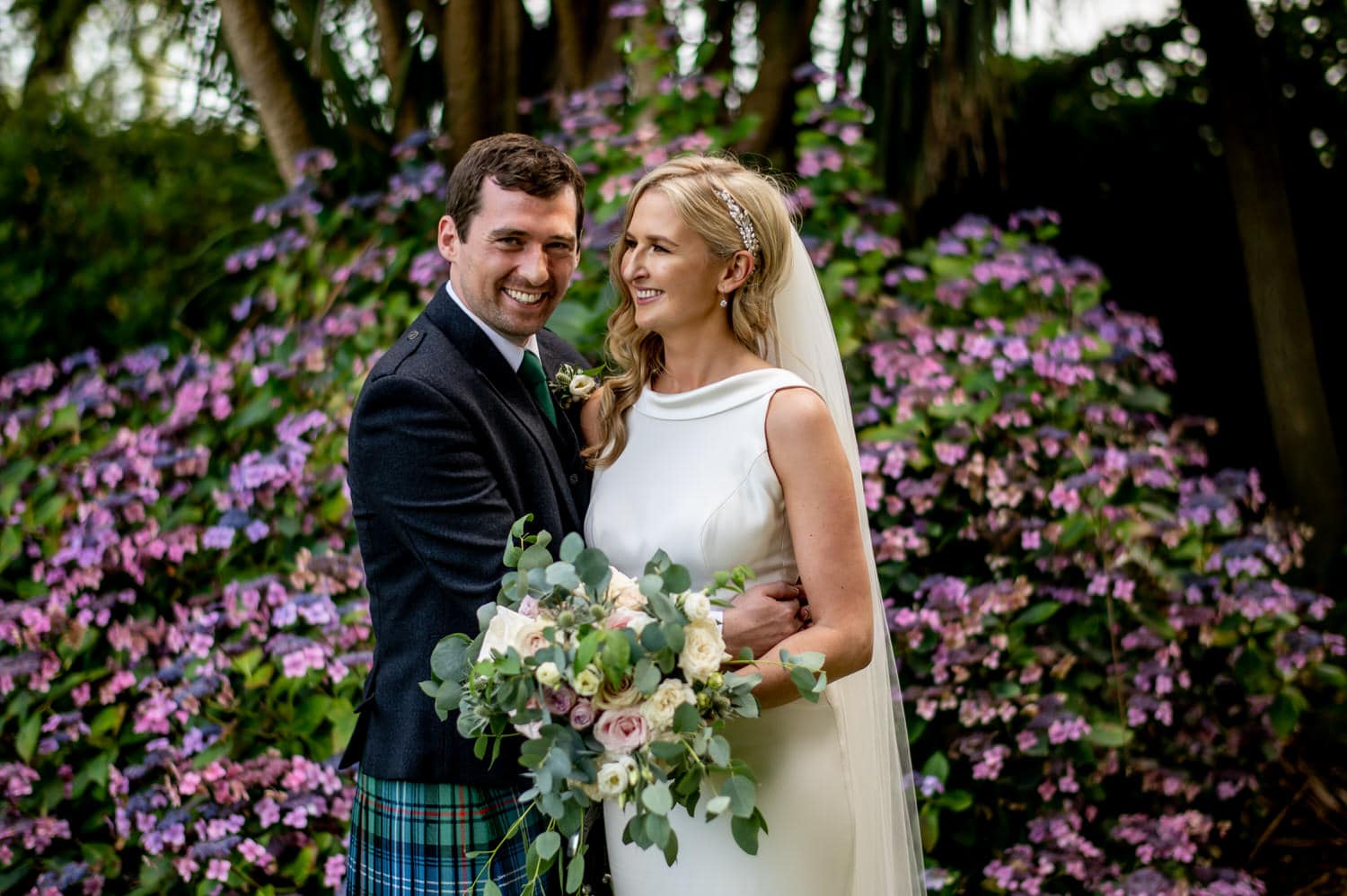 Married couple smiling at Tinakilly Country House Hotel in front of a purple bush.